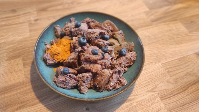Schüssel mit braunem Fleisch, blauen Beeren und einer orangefarbenen Garnitur.